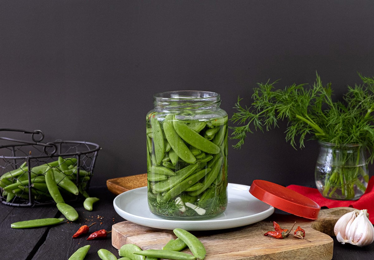 Pickled snap peas in a jar on a white plate.