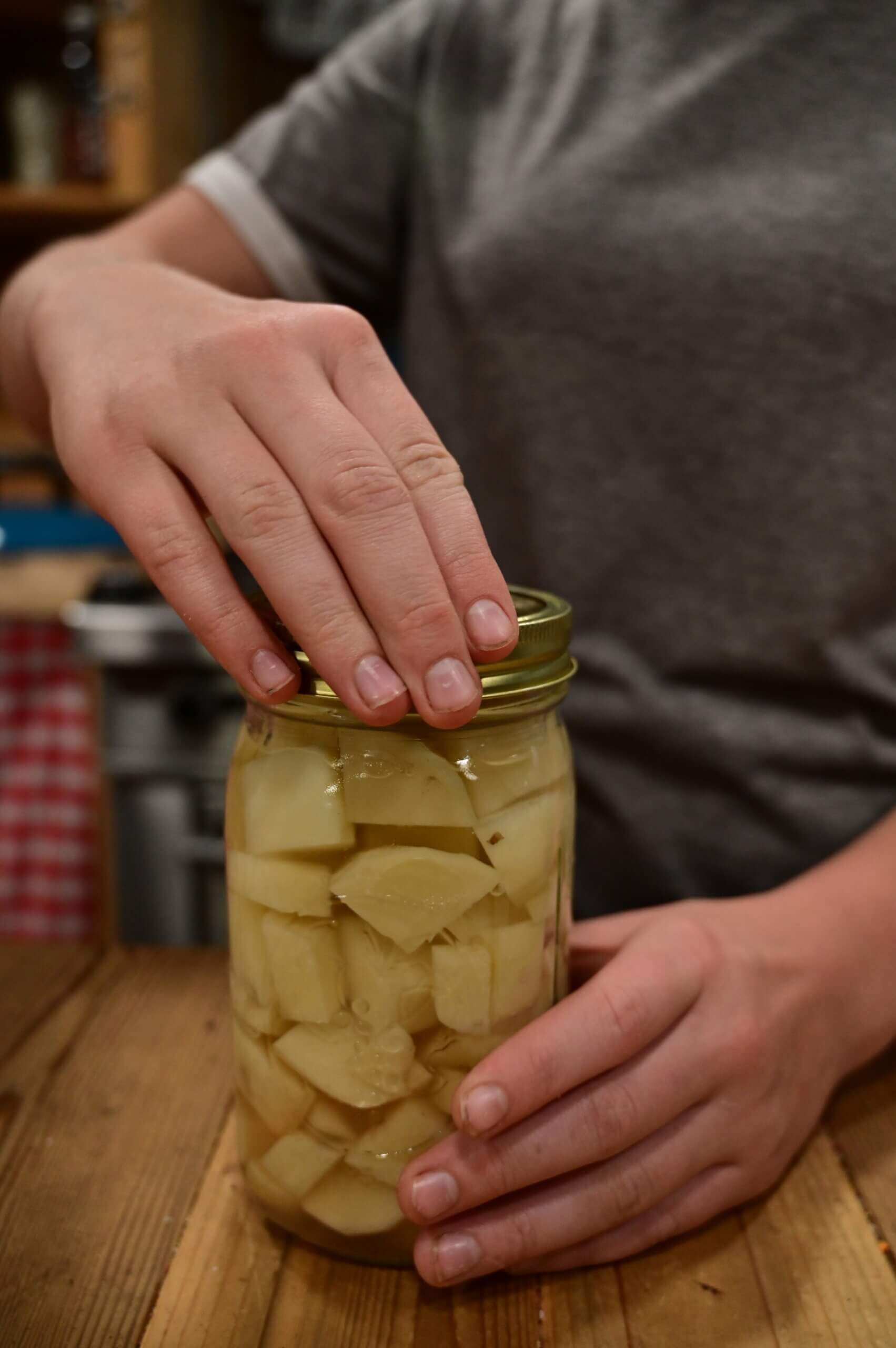 Adding a lid to a jar of potatoes ready to can.