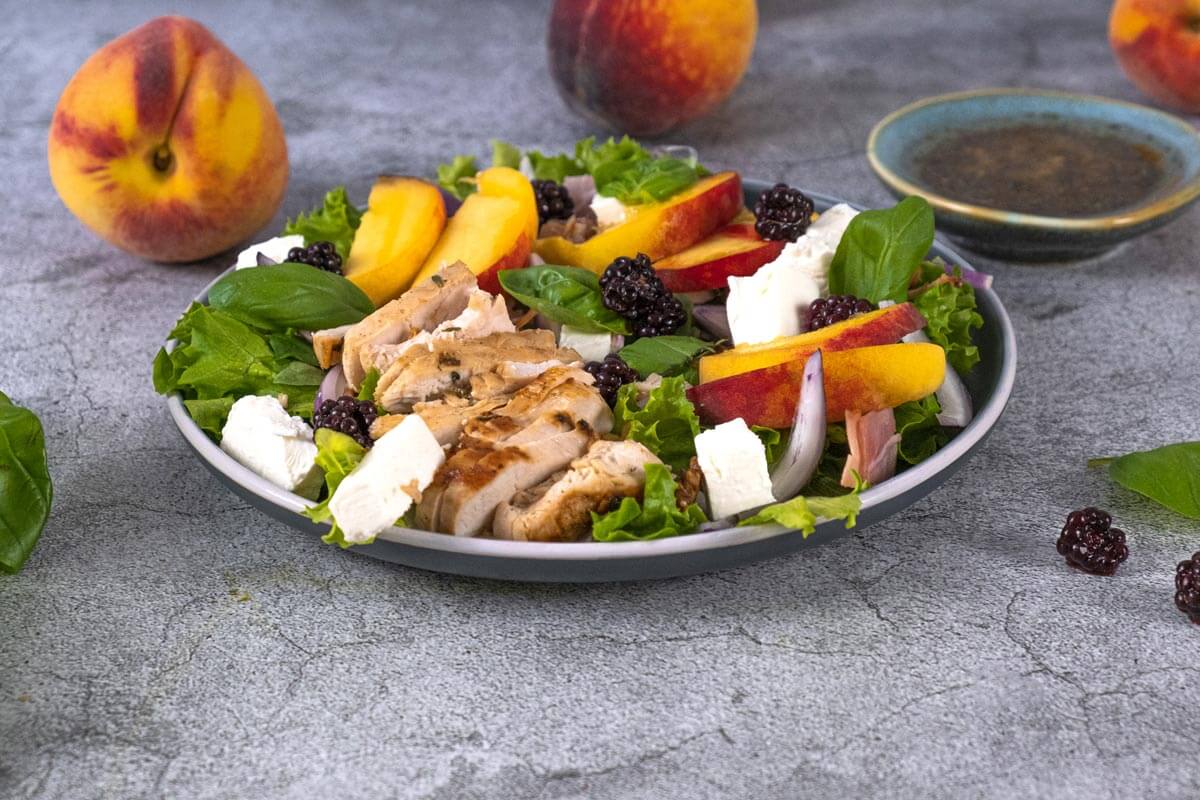 Peach salad dished on a plate with chicken, nuts and other items.