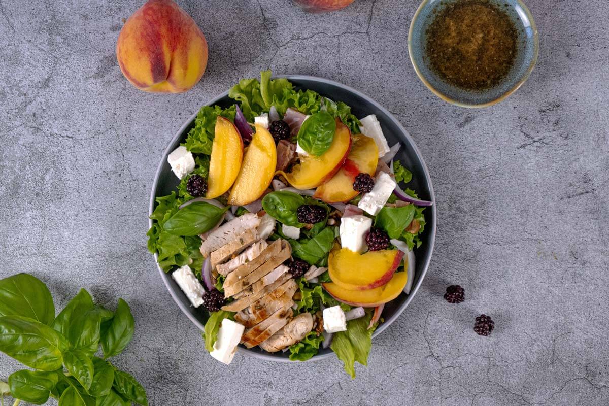 Peach salad dished on a plate with chicken, nuts and other items.