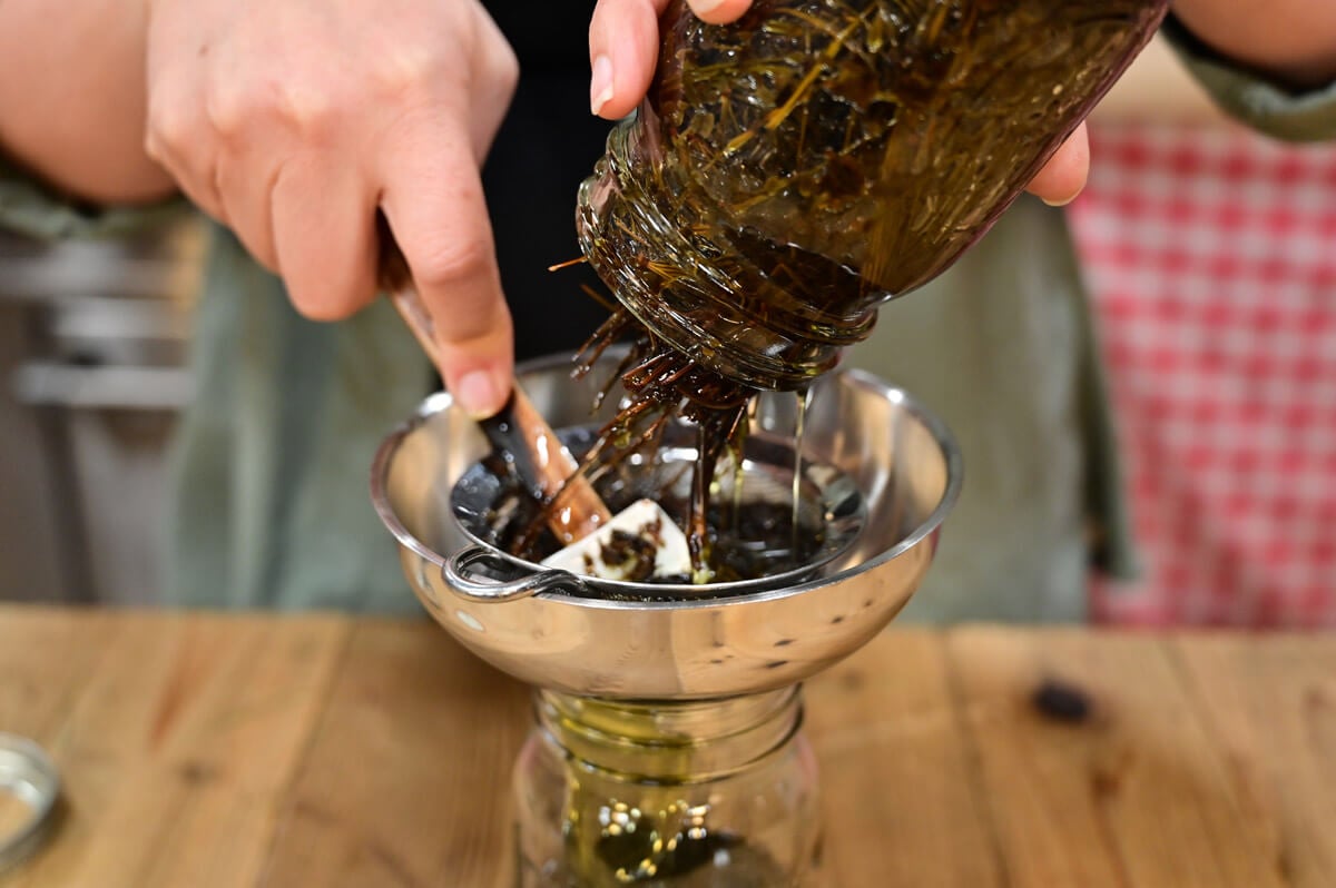 A woman straining a jar of herbal pine oil.