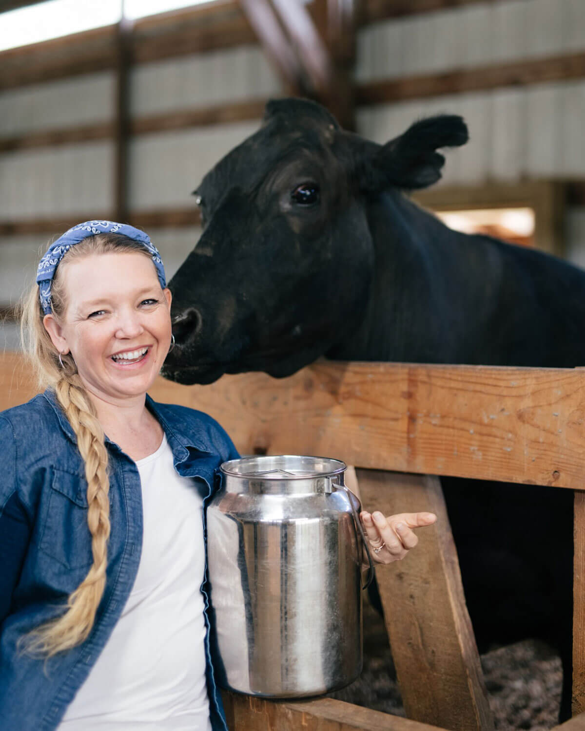 A woman standing next to a black milk cow holding a stainless steel tub of fresh milk.