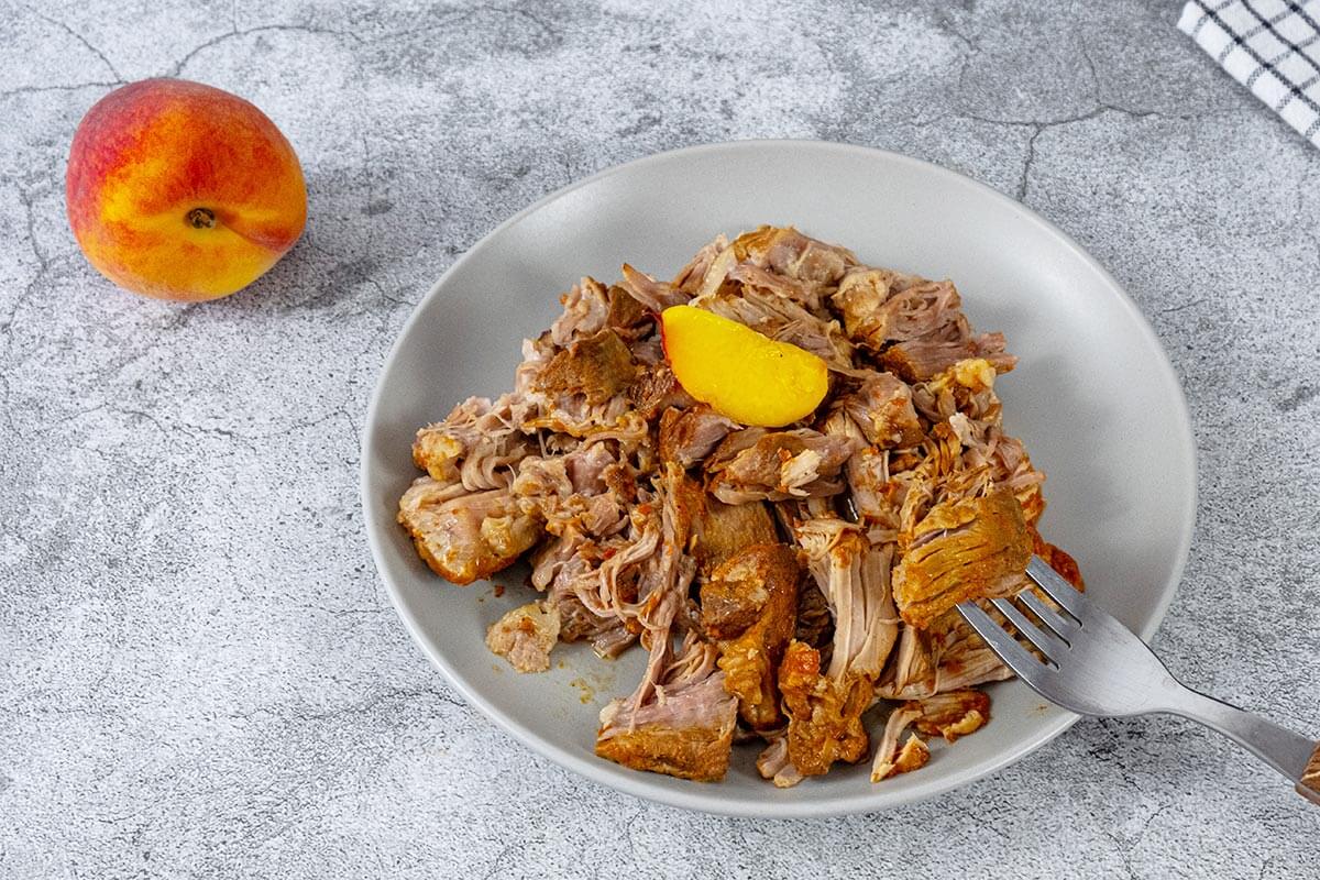 BBQ pulled pork on a white plate with a peach slice on top.