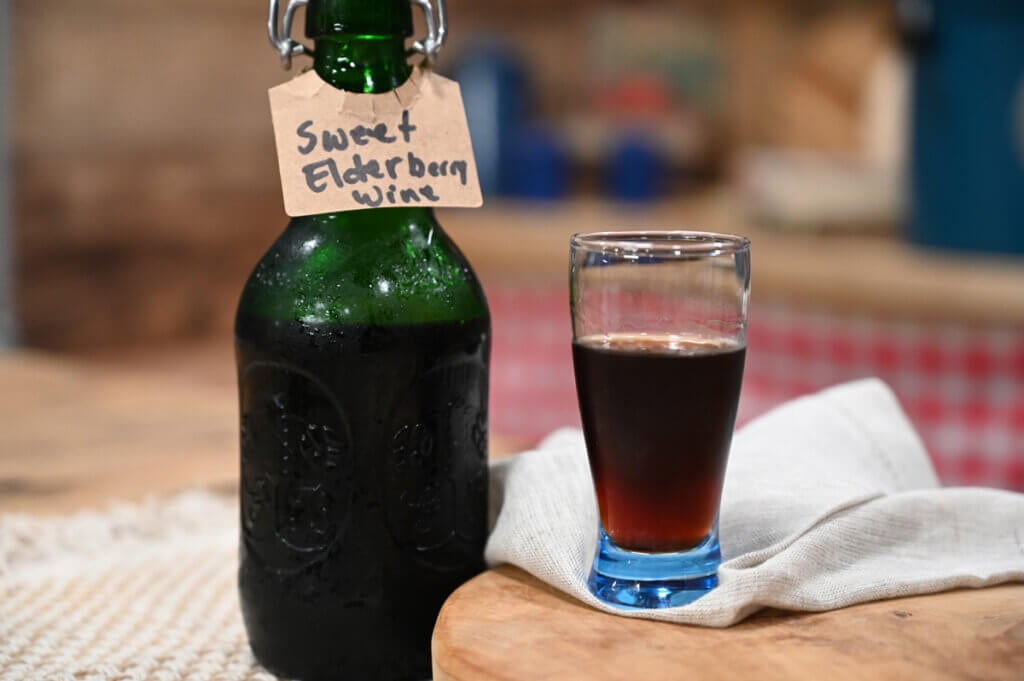 A bottle of sweet elderberry wine with a glass poured next to it.