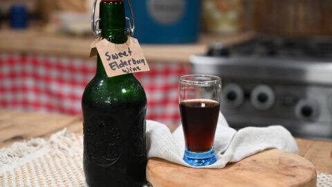 A bottle of sweet elderberry wine with a glass poured next to it.
