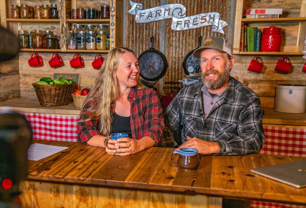 A man and woman sitting at a table with a camera filming them.