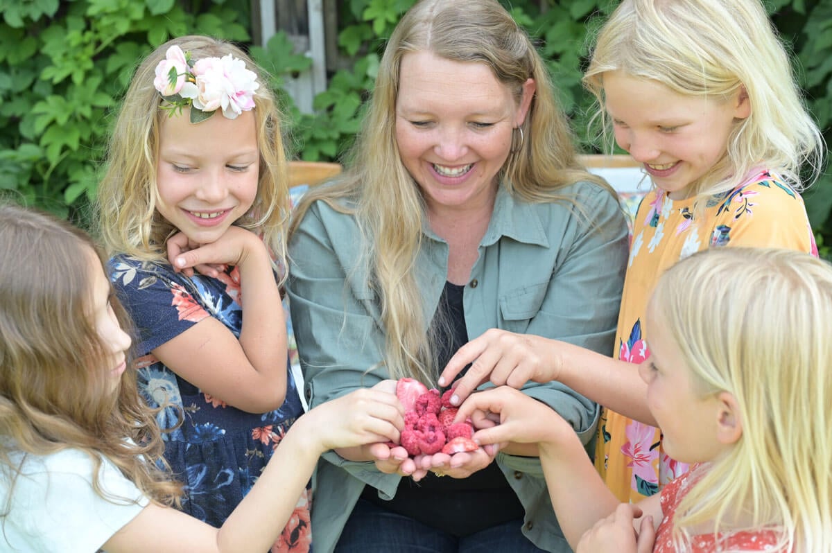 A woman with four girls giving them freeze dried raspberries.