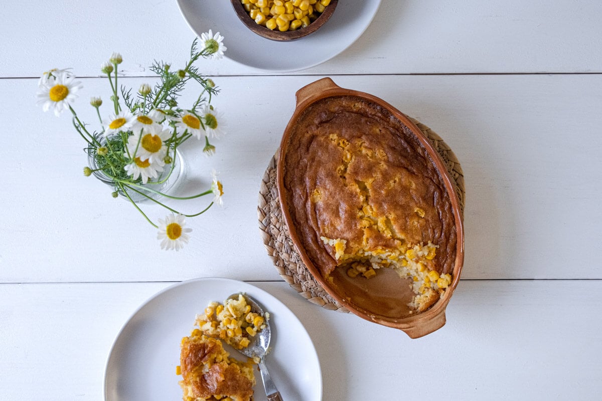 Overhead shot of corn pudding in a casserole dish with some dished up on a white plate.
