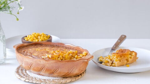 Corn pudding in a casserole dish with a serving on a white plate.