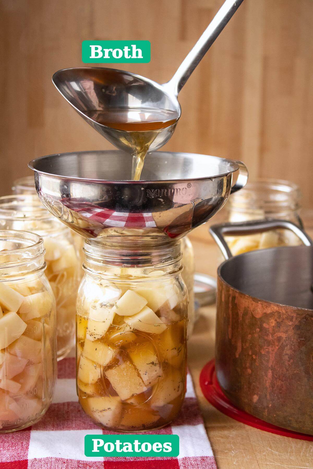 Broth poured from a ladle through a metal funnel into a glass jar filled with potato chunks.