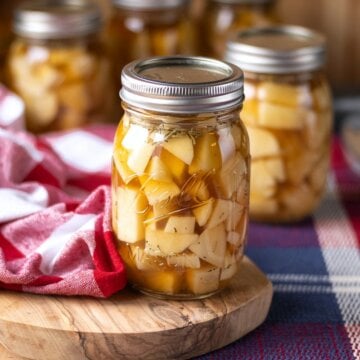 Lidded jar of potato chunks in golden broth on a wooden board, with additional jars behind it.