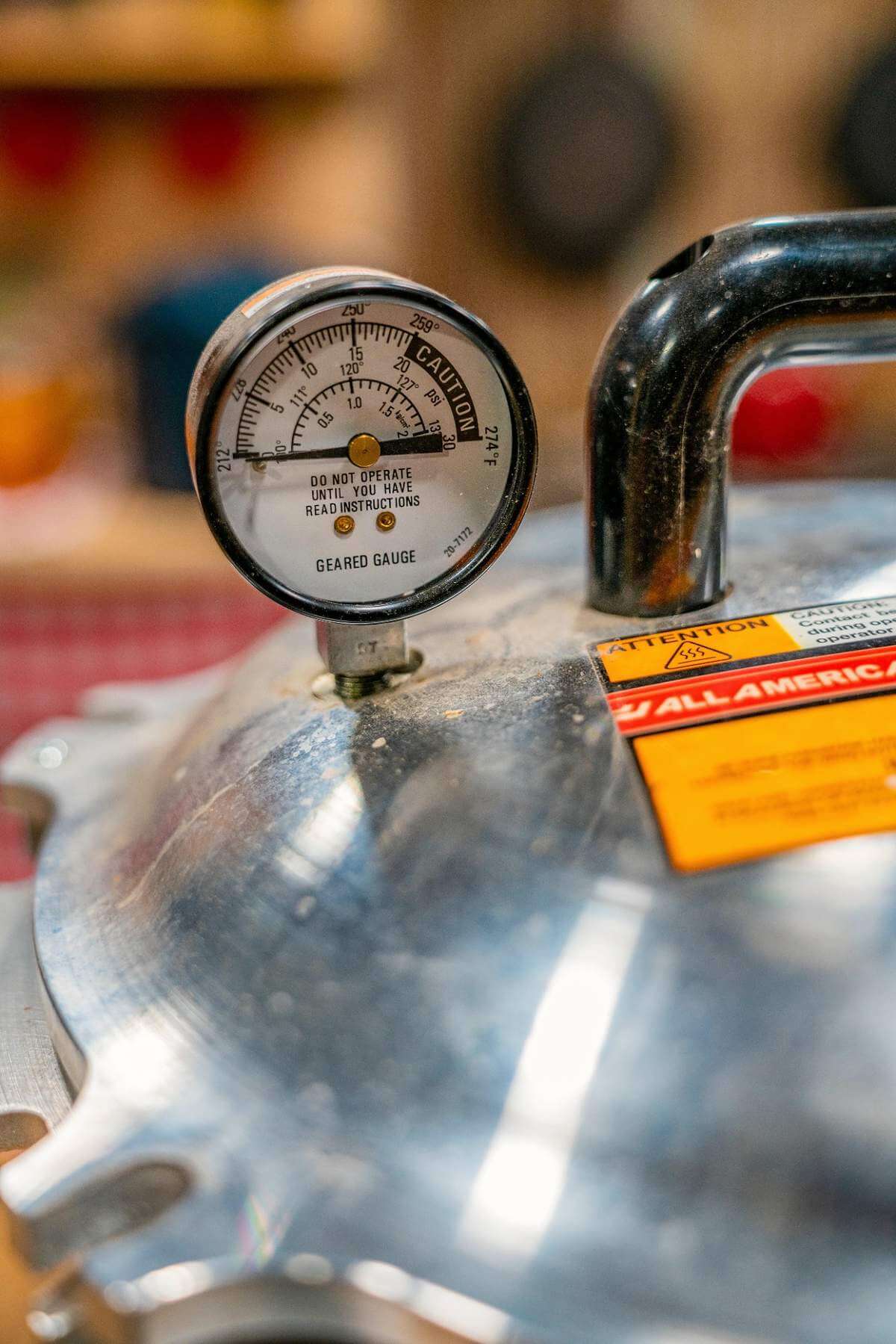 Close-up of a pressure canner dial gauge beside the black lid handle.