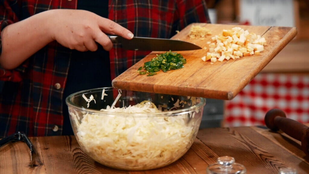 Jalapenos, apples and ginger going into a bowl of cabbage.