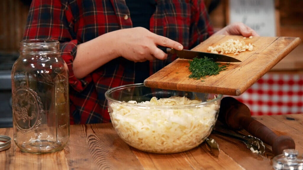 Dill and garlic being added to a bowl of cabbage.