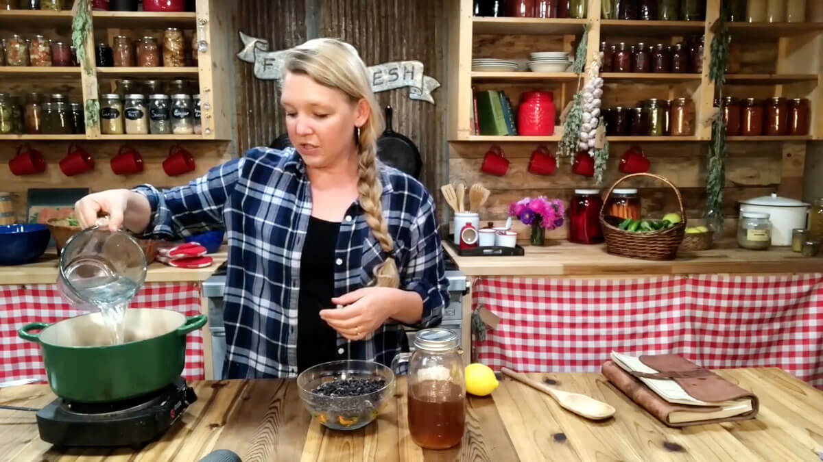 A woman adding elderberry syrup ingredients to a Dutch oven.
