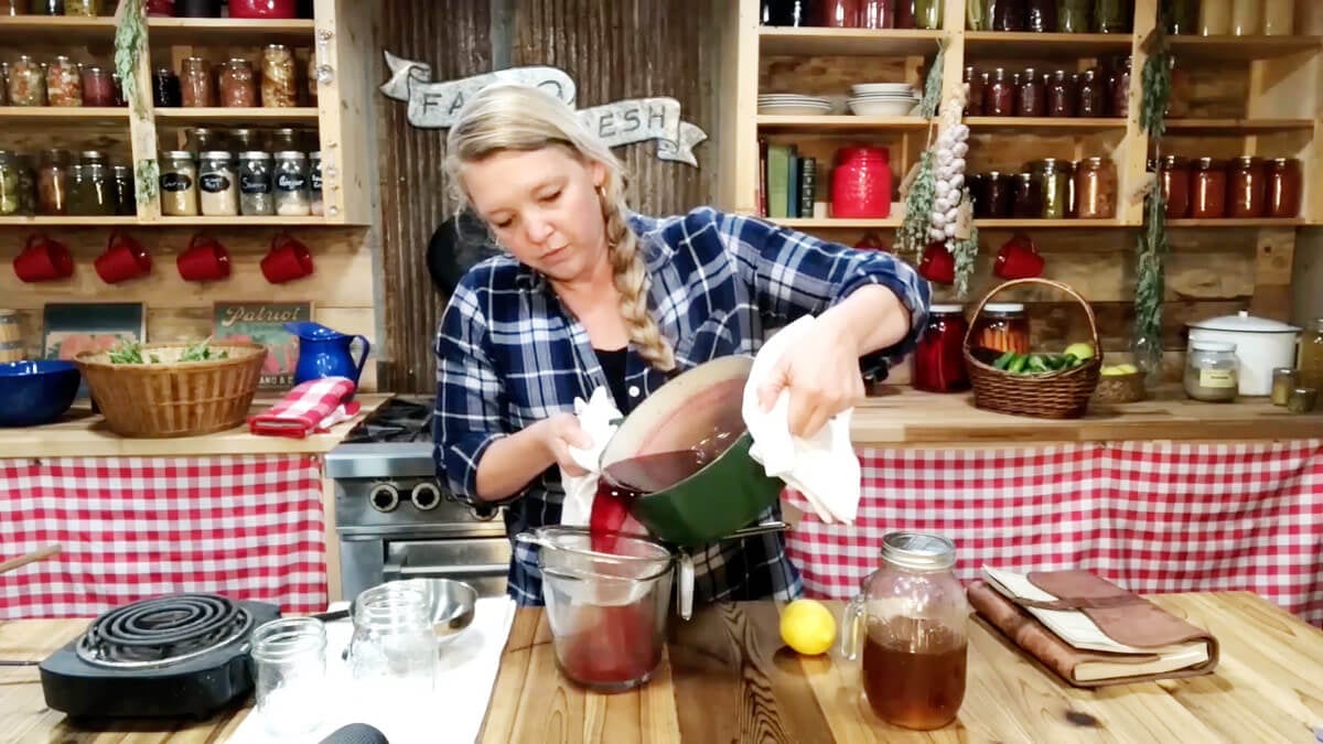 A woman straining cooked elderberries through a mesh strainer.