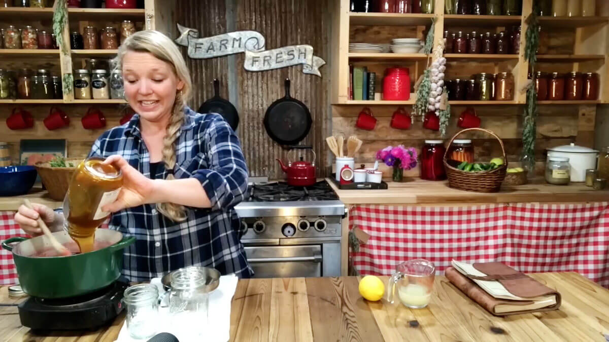 A woman adding honey and lemon juice to a Dutch oven filled with elderberry syrup.