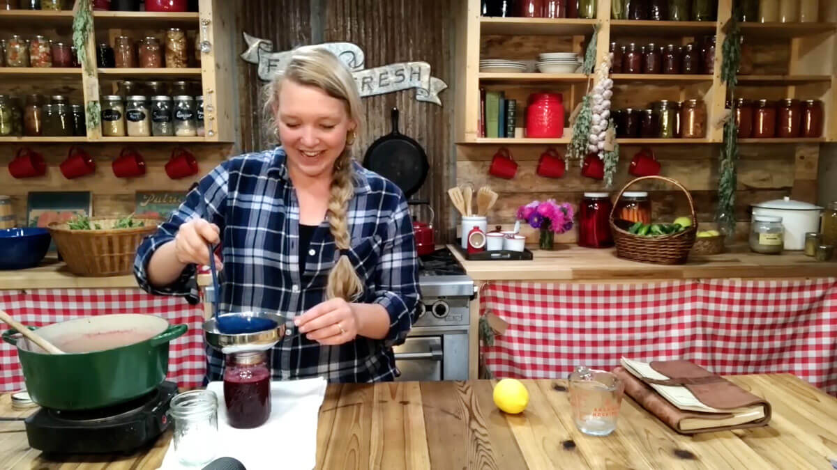 A woman ladling elderberry syrup into a mason jar.