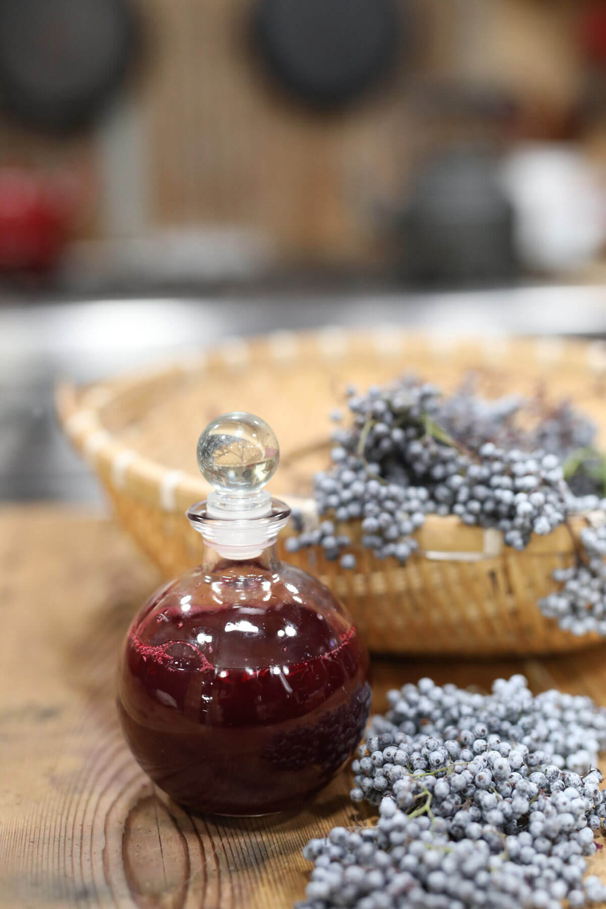 A basket full of fresh elderberries sitting next to a bottle of homemade elderberry syrup.