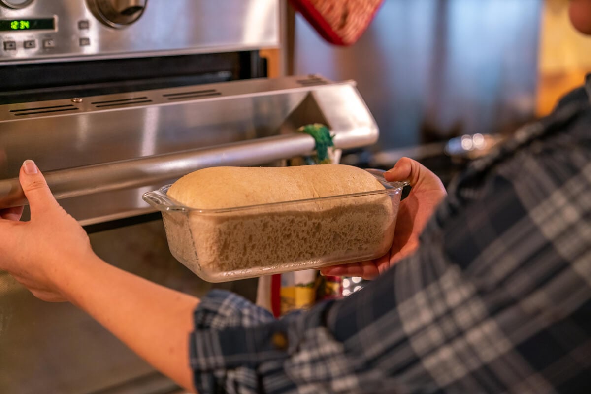 A woman placing a risen loaf of bread into the oven to bake.