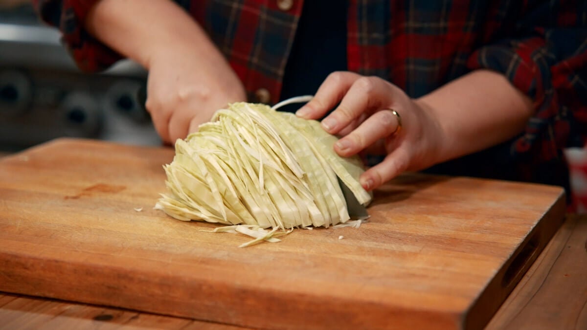 Cabbage being sliced on a cutting board.