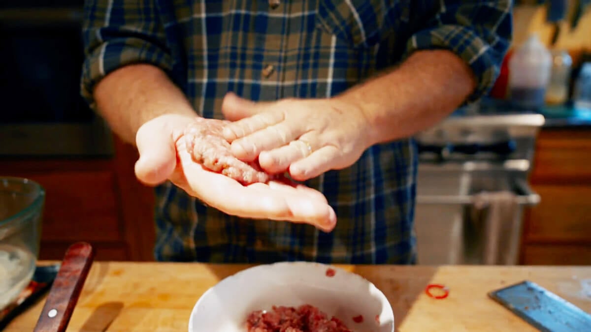 A man pressing ground pork breakfast sausage into a patty.