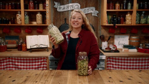 A woman holding up a jar of alfalfa sprouts.