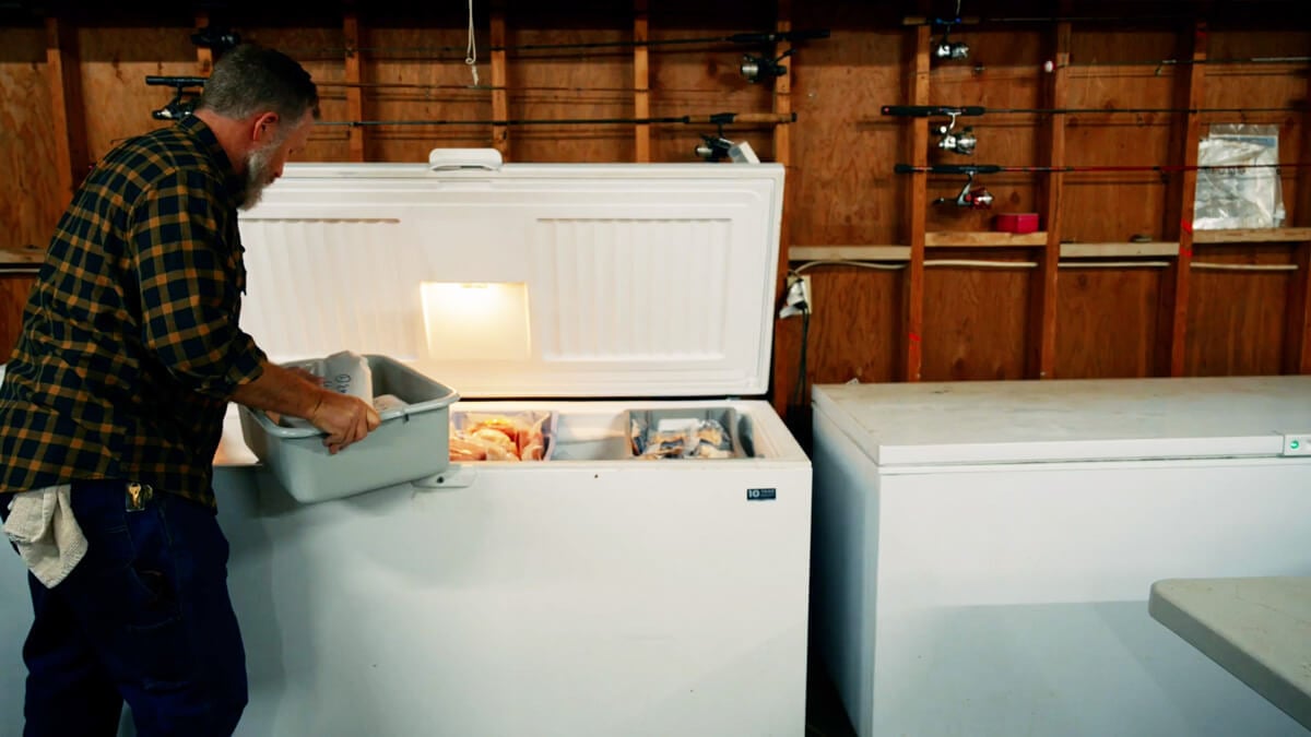 A man loading a chest freezer with pork products.