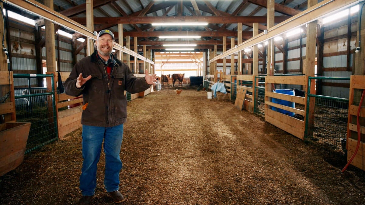 A man standing in the breezeway of a large barn.