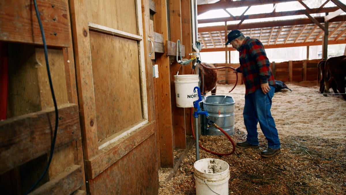 A man adding water to a trough inside a barn.