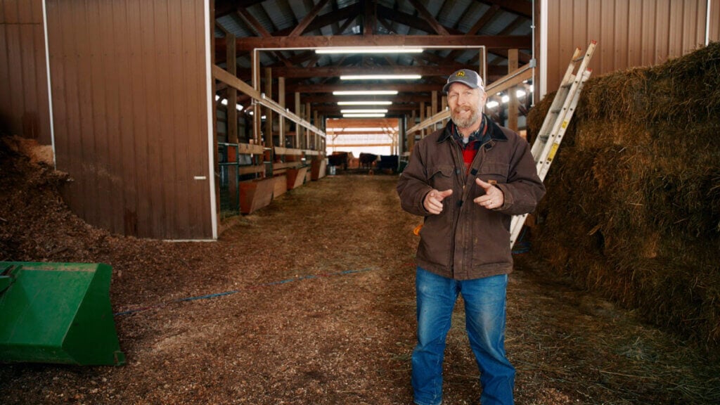 A man standing just outside a large barn.