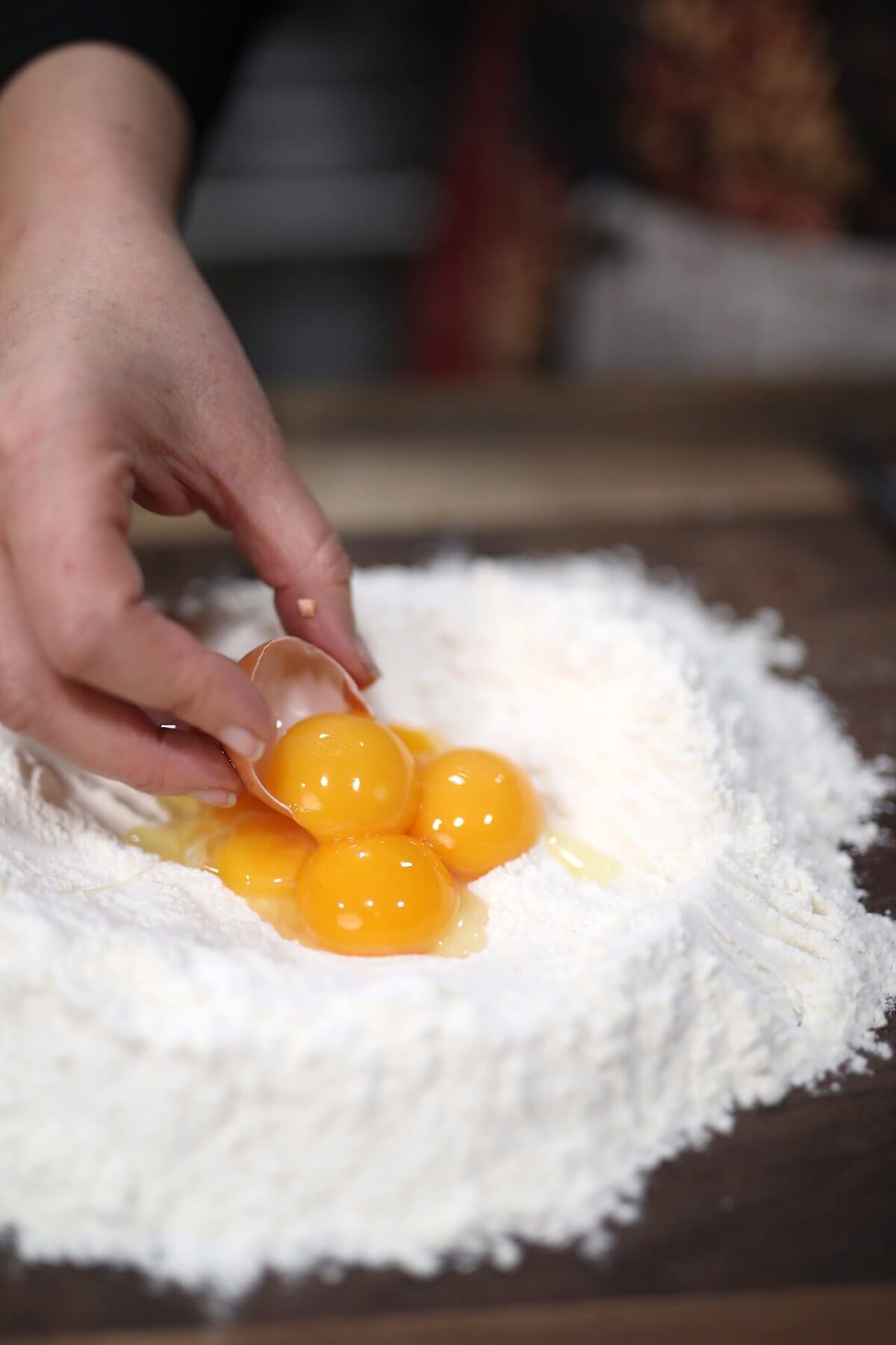 Adding eggs to a well in a mound of flour on a wooden board.