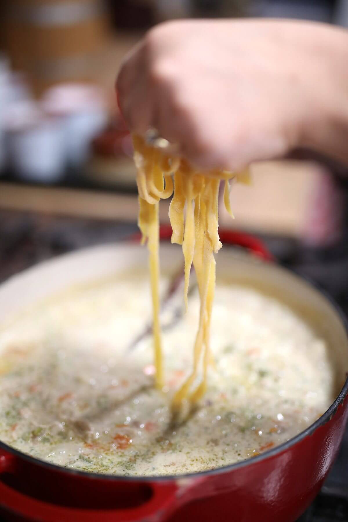 Lowering fresh egg noodles into a pot of simmering soup.