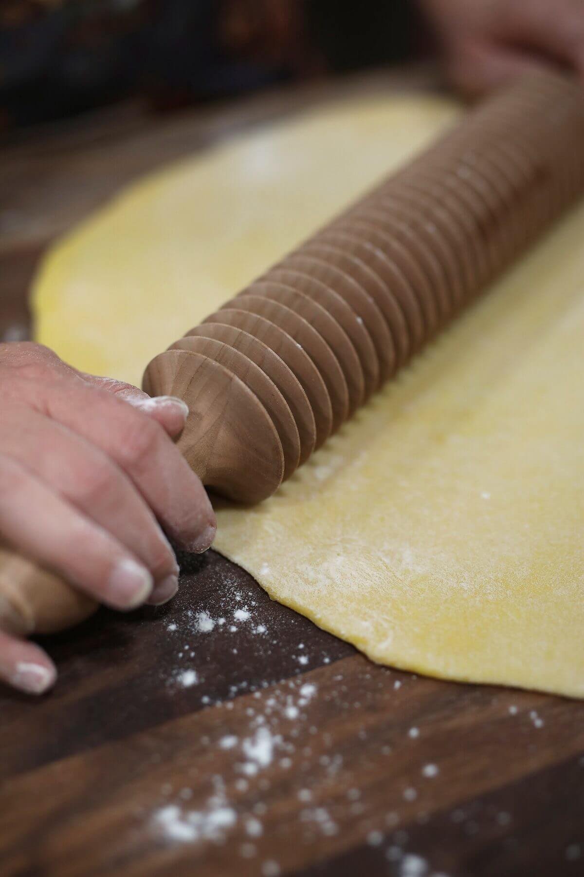 Cutting rolled egg noodle dough with a grooved wooden noodle cutter.