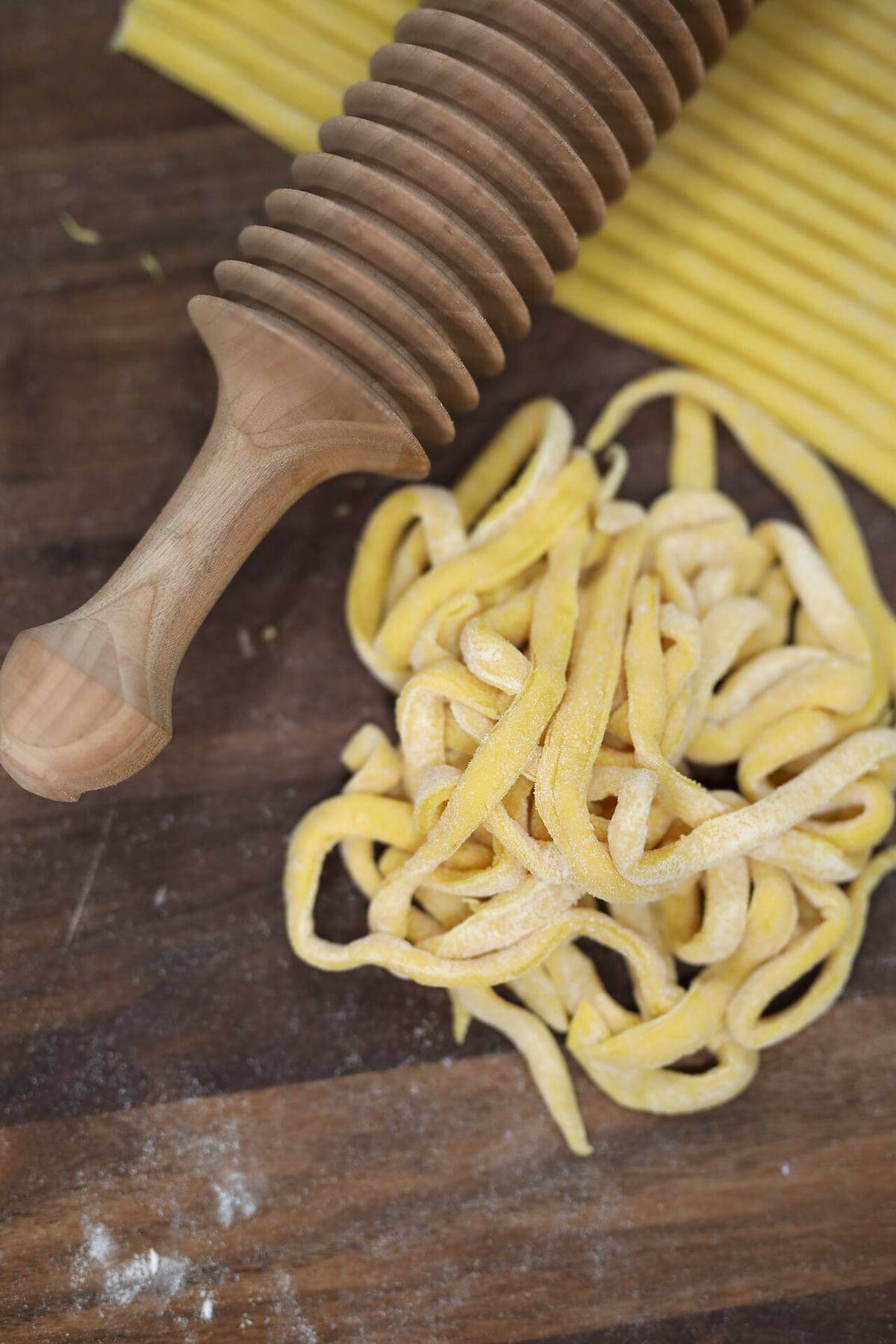 Freshly cut egg noodles beside a wooden noodle cutter on a floured board.