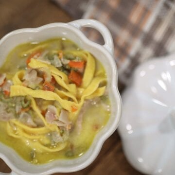 Homemade egg noodles in a white bowl of soup with meat, carrots, and celery.