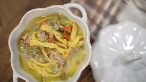 Homemade egg noodles in a white bowl of soup with meat, carrots, and celery.
