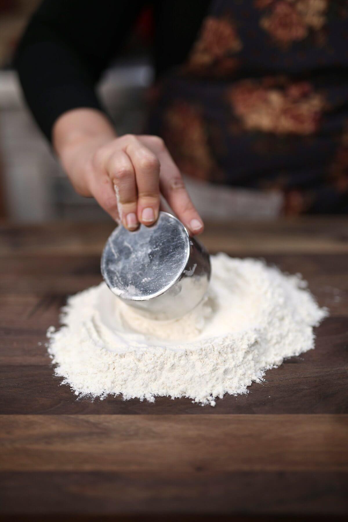 Measuring flour onto a wooden work surface for homemade egg noodles.