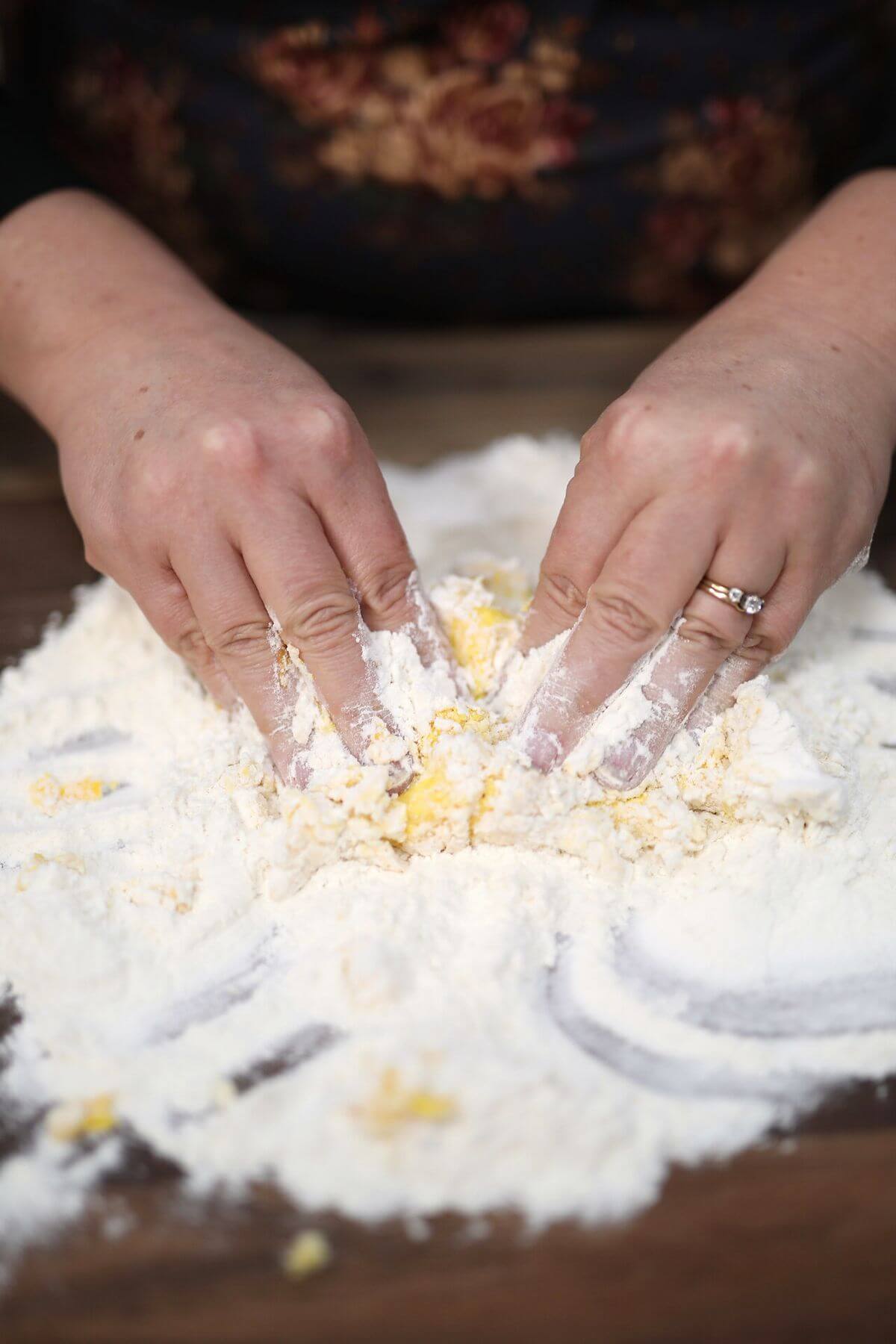Mixing eggs and flour by hand on a wooden work surface.