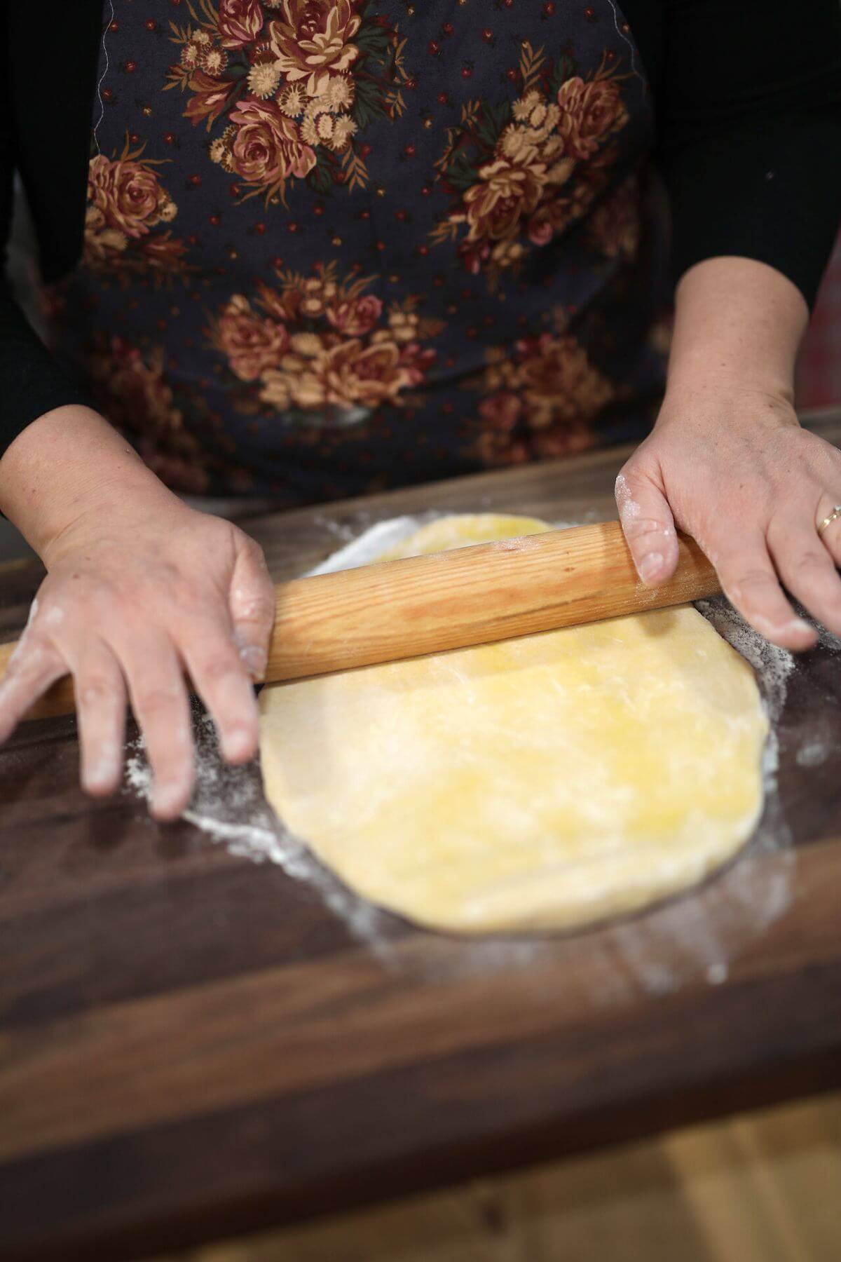 Rolling egg noodle dough flat with a wooden rolling pin.