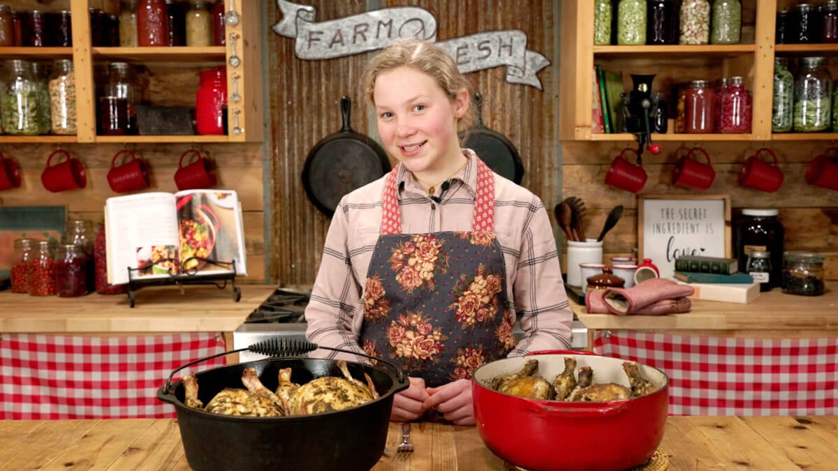 A young girl in the kitchen with two whole roasted chickens on the counter.