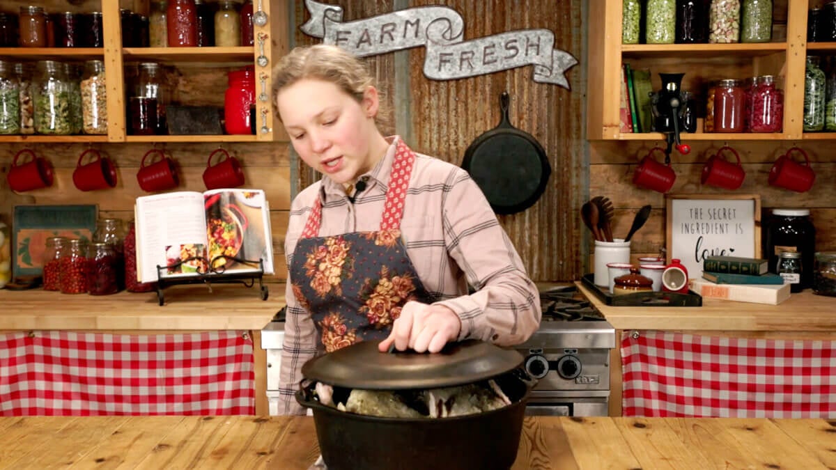 A young girl placing the lid on a pot with whole chickens inside.