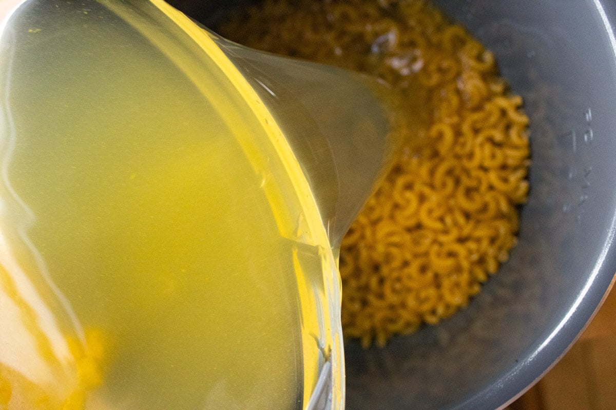 Broth being added to uncooked macaroni noodles in an Instant Pot.