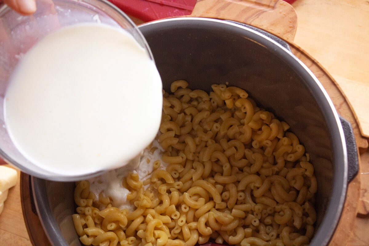 Cream being added to an Instant Pot with cooked macaroni noodles inside.
