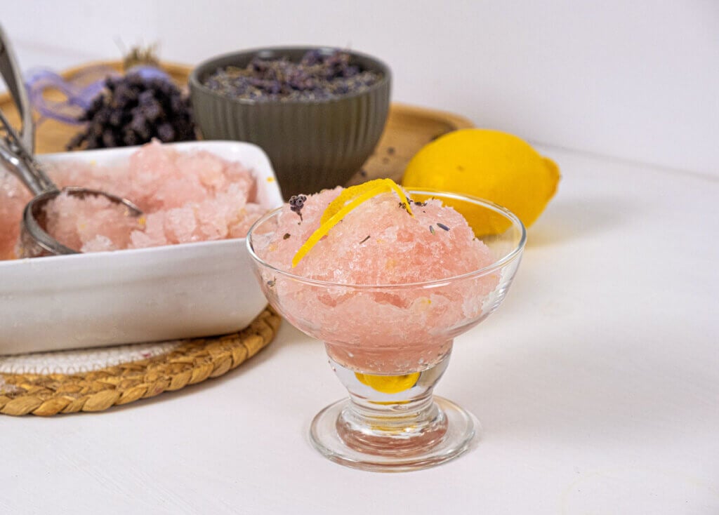 Lemon sorbet served in a glass with lemon zest and lavender on top.