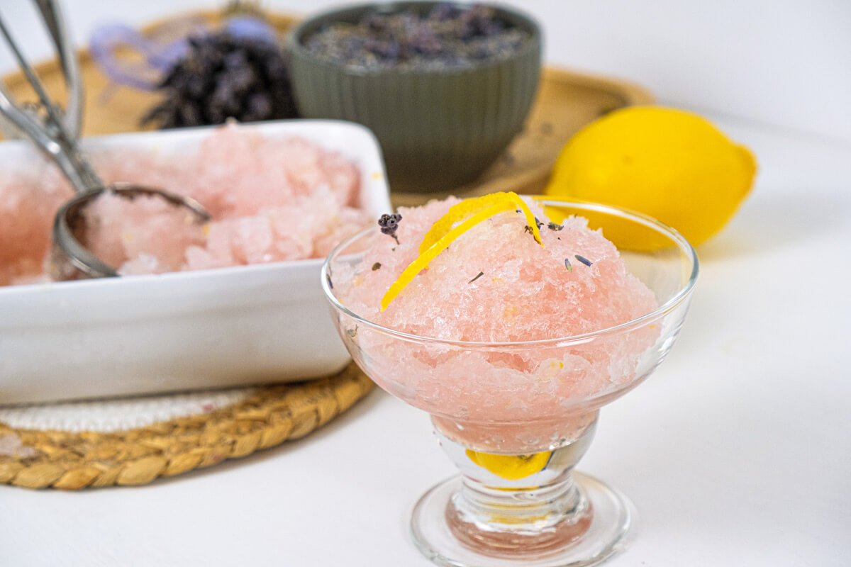 Lemon sorbet served in a glass with lemon zest and lavender on top.