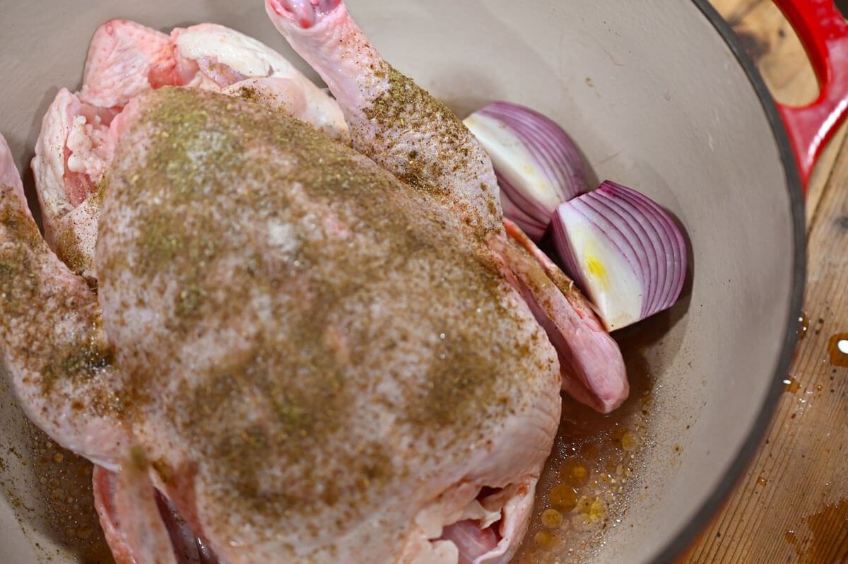 A whole chicken in a Dutch oven with red onions nestled beside it.