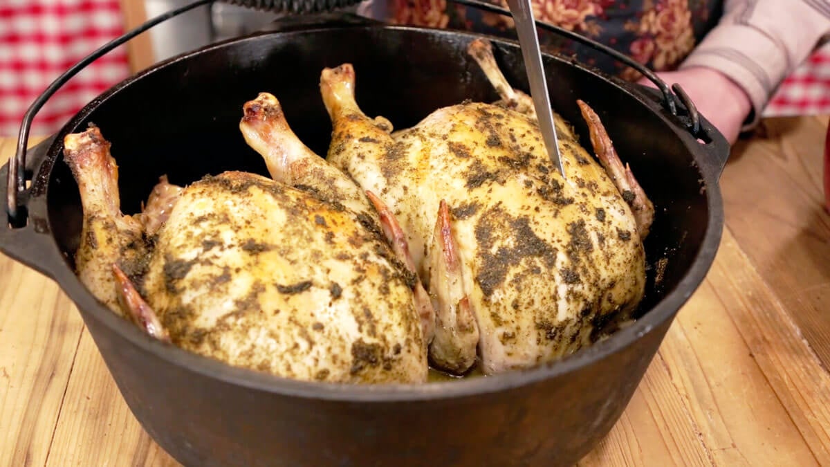 Two whole roasted chickens in a deep cast iron pan.