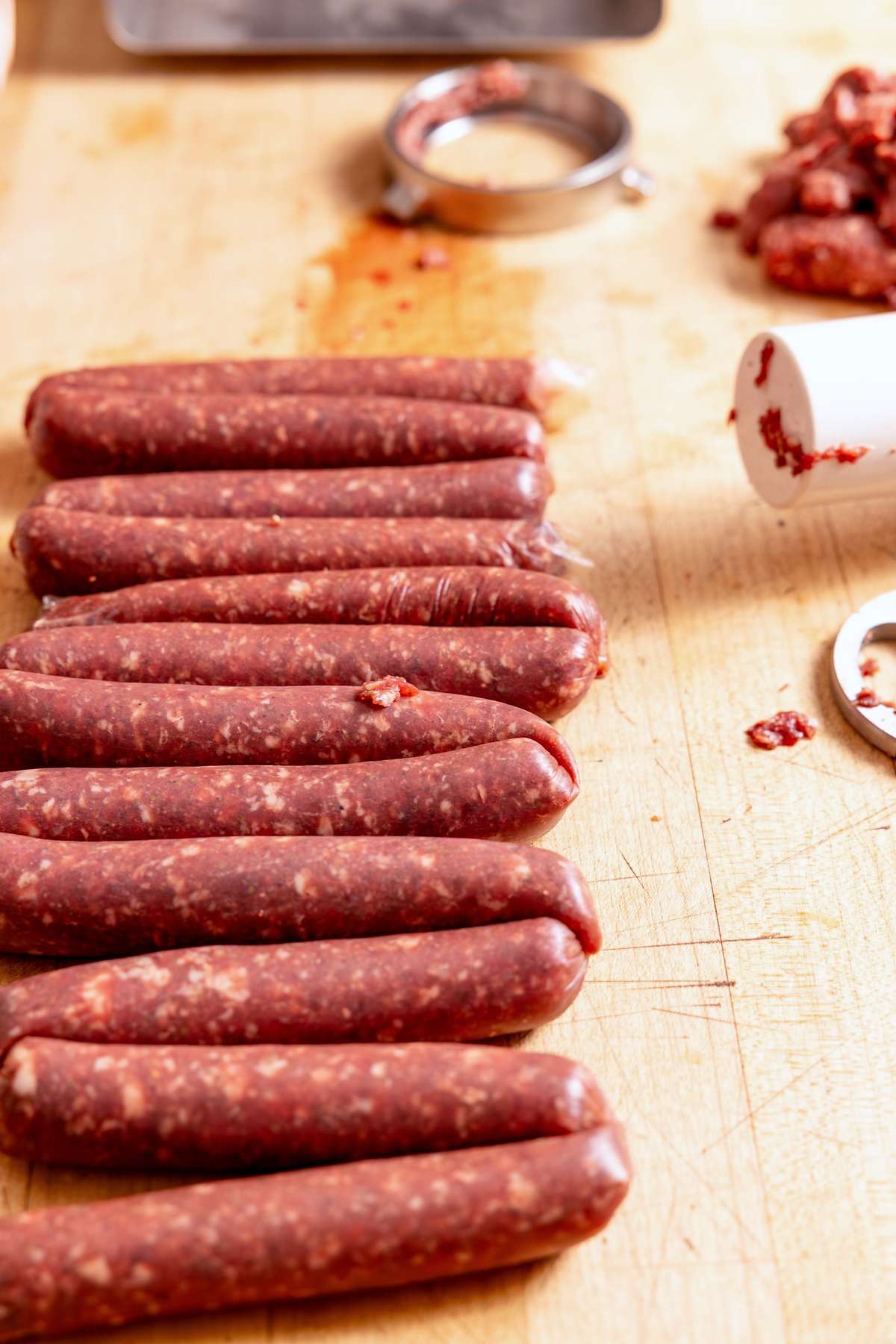 Fresh uncooked wild game sausage links lined up on a wooden worktop.