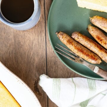 Overhead view of sausage links, cornbread and coffee on a wooden table.